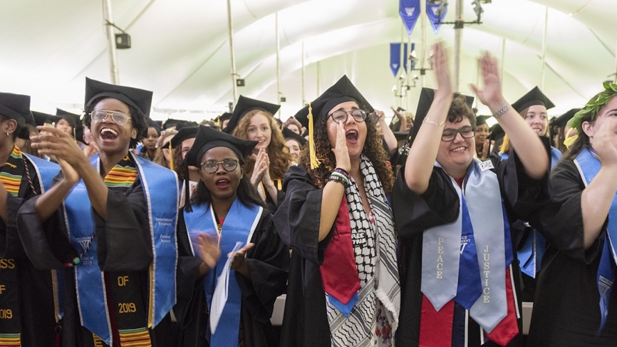 Students cheer under a large tent during commencement 2019