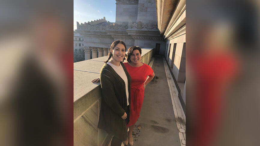 Two women stand in front of a white building.