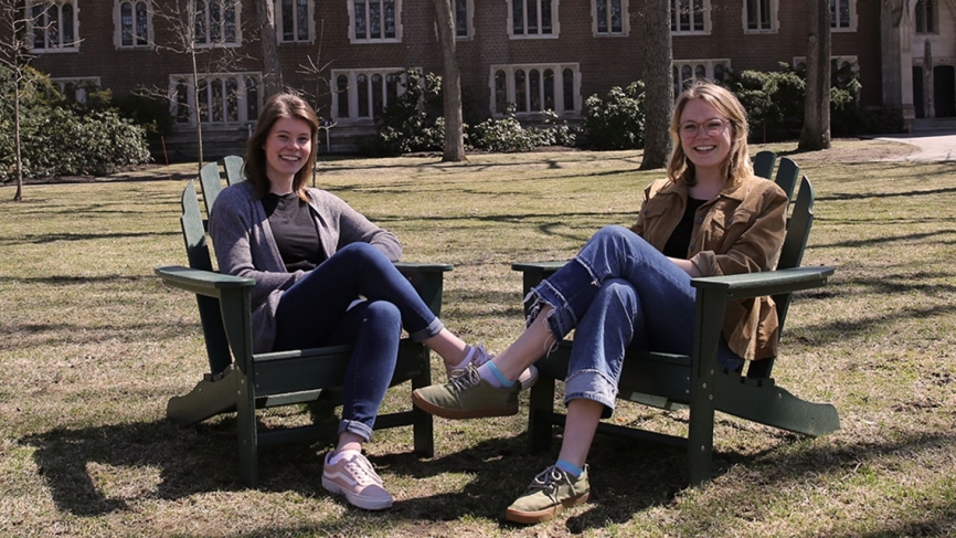 Two students sit in chairs on the academic quad