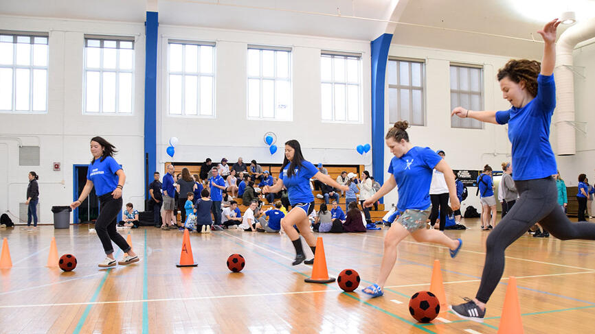Students kick soccer balls inside a gym
