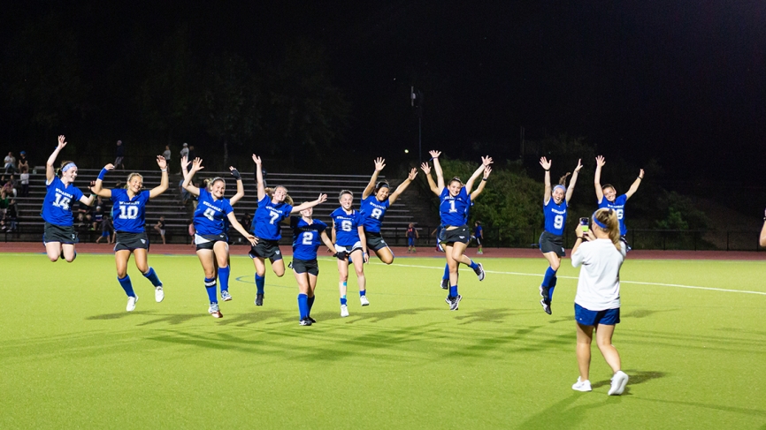 The Wellesley Field Hockey team jumps during a night game under the lights.