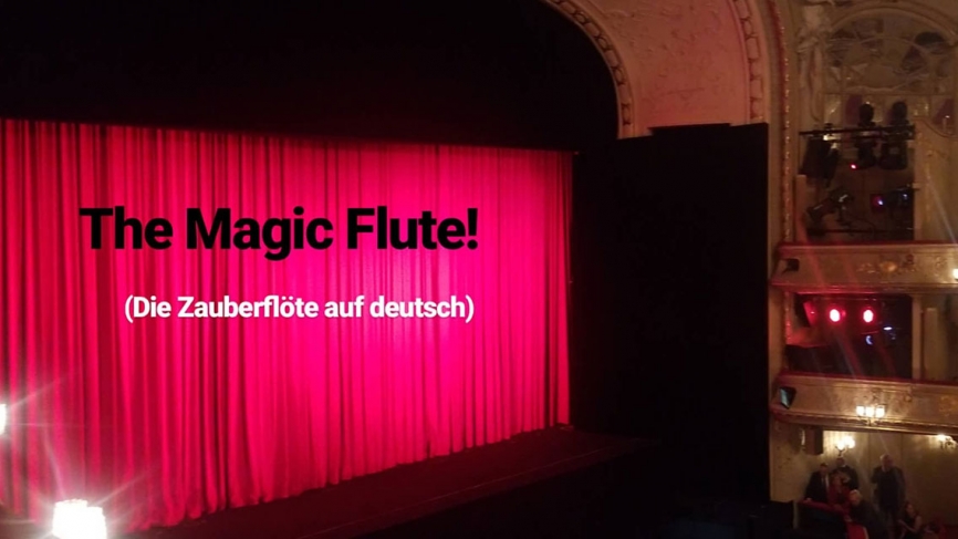 The stage at the Berlin State Opera with a closed red curtain. Text reads, "Magic Flute” (Die Zauberflöte auf deutsch)