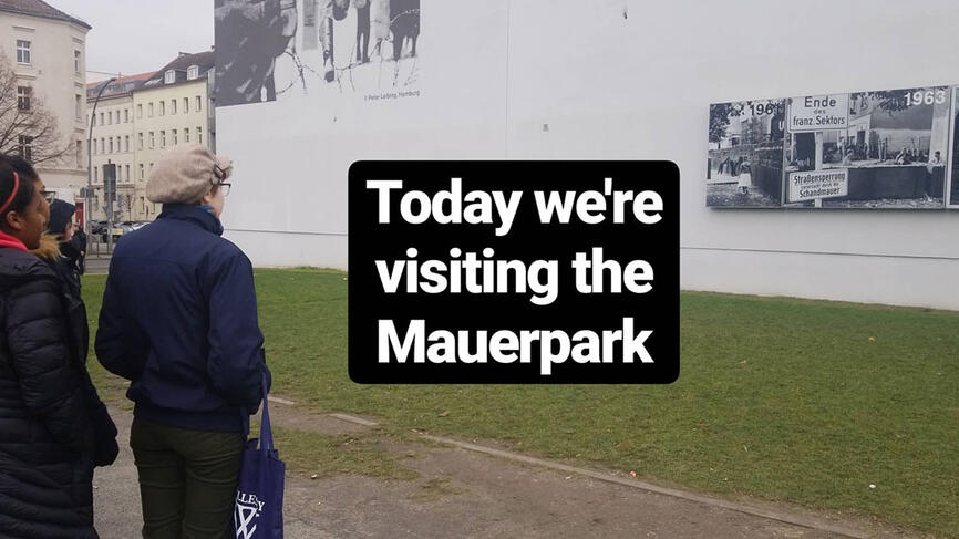 Students outside at Mauerpark look at a long wall with black and white photos. Text reads, Today we're visiting the Mauerpark