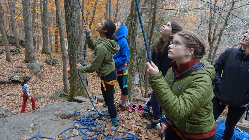 Students hold onto ropes before beginning to climb a boulder outdoors.