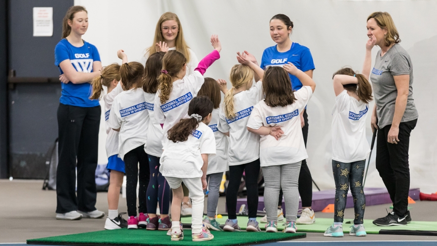 A group of young girls stand with Wellesley student athletes and a coach