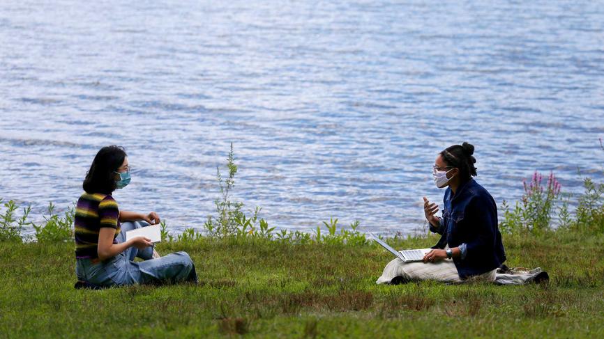 two students sitting by the lake reading books and talking