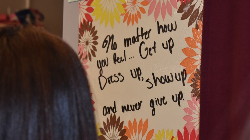 A student looks at a sign on a wall that reads, "No matter how you feel, get up, dress up, show up, and never give up."