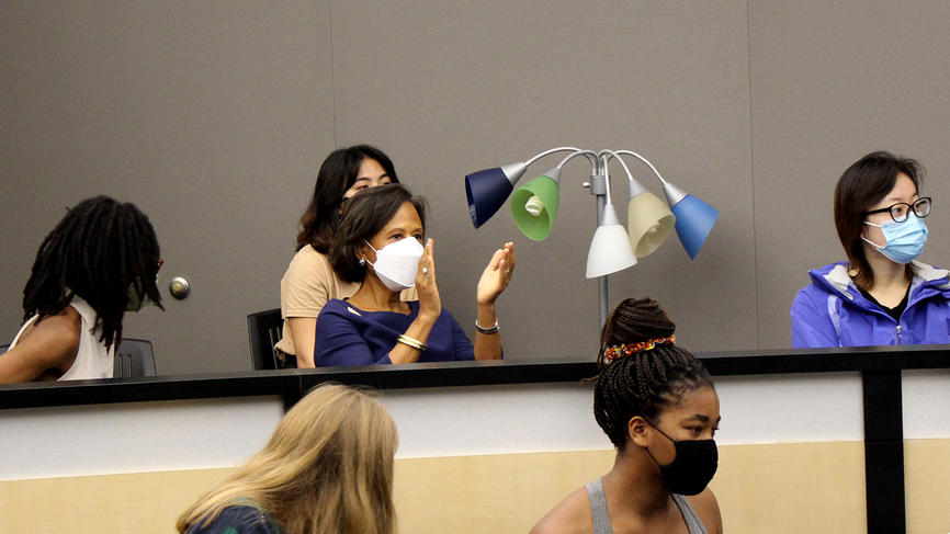 President Paula Johnson wears a mask while attending a Tanner presentation and is seen mid-clap in the photo.