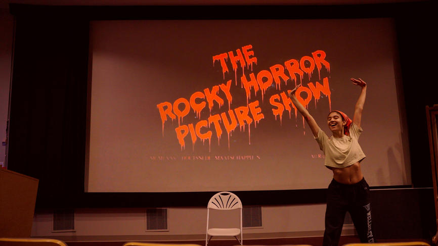 A student practices a dance on stage in front of a screen that reads The Rocky Horror Picture Show