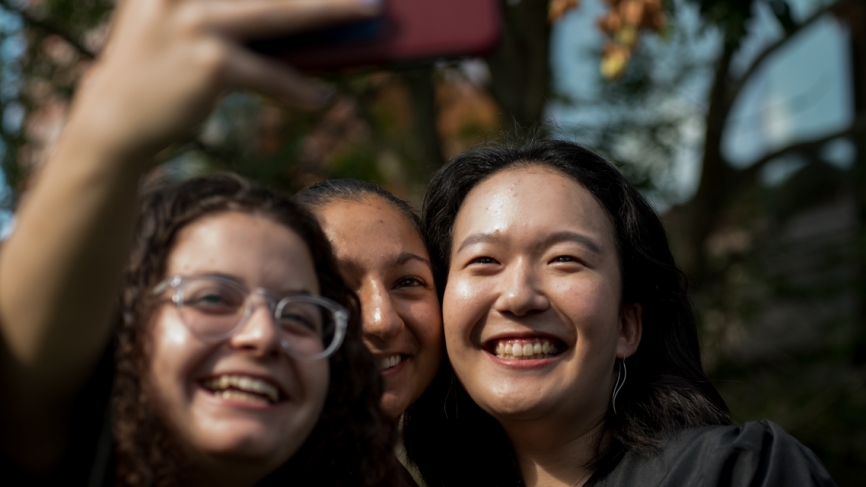 Three students celebrate Convocation with a selfie in front of Alumnae Auditorium. 