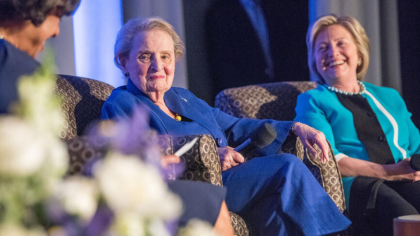 Hillary Clinton and Madeleine Albright sit on a stage with President Johnson