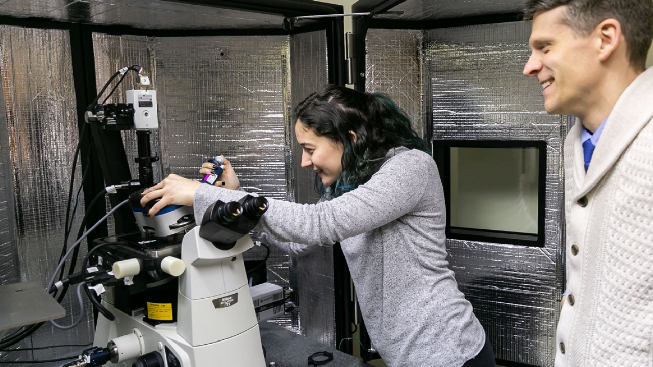 A student works with a microscope as a professor looks on