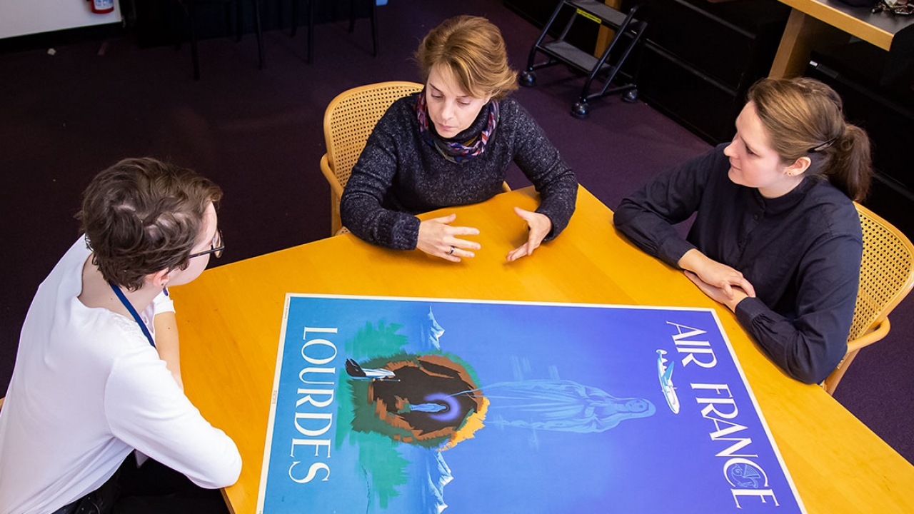 Three people look at a blue poster depicting the Virgin Mary