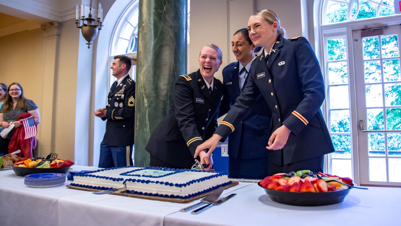 Three ROTC cadets cut a cake with  a saber