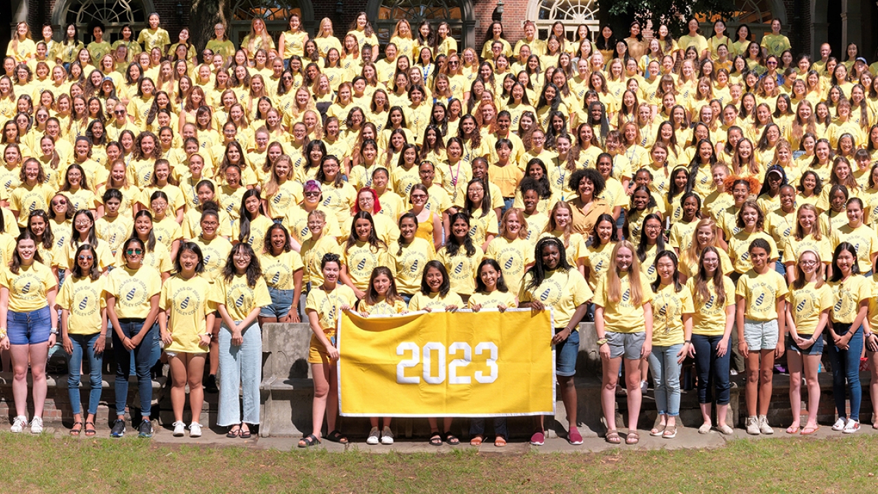 The class of 2023's class photo. They wear yellow shirts and hold a yellow banner.