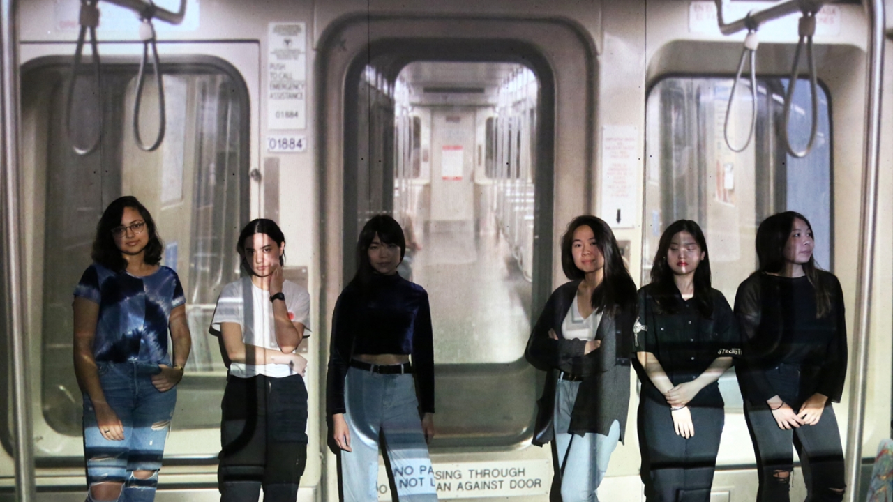 Six students stand in front of an art installation that depicts the inside of the MBTA's Red Line.