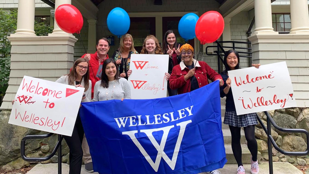 A group of students and admissions officers stand outside the admissions building with signs and balloons.