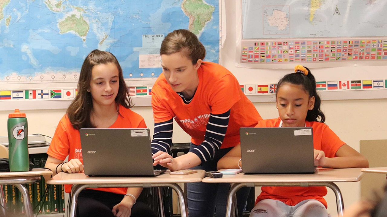 A professor works with two middle school female students at computers.