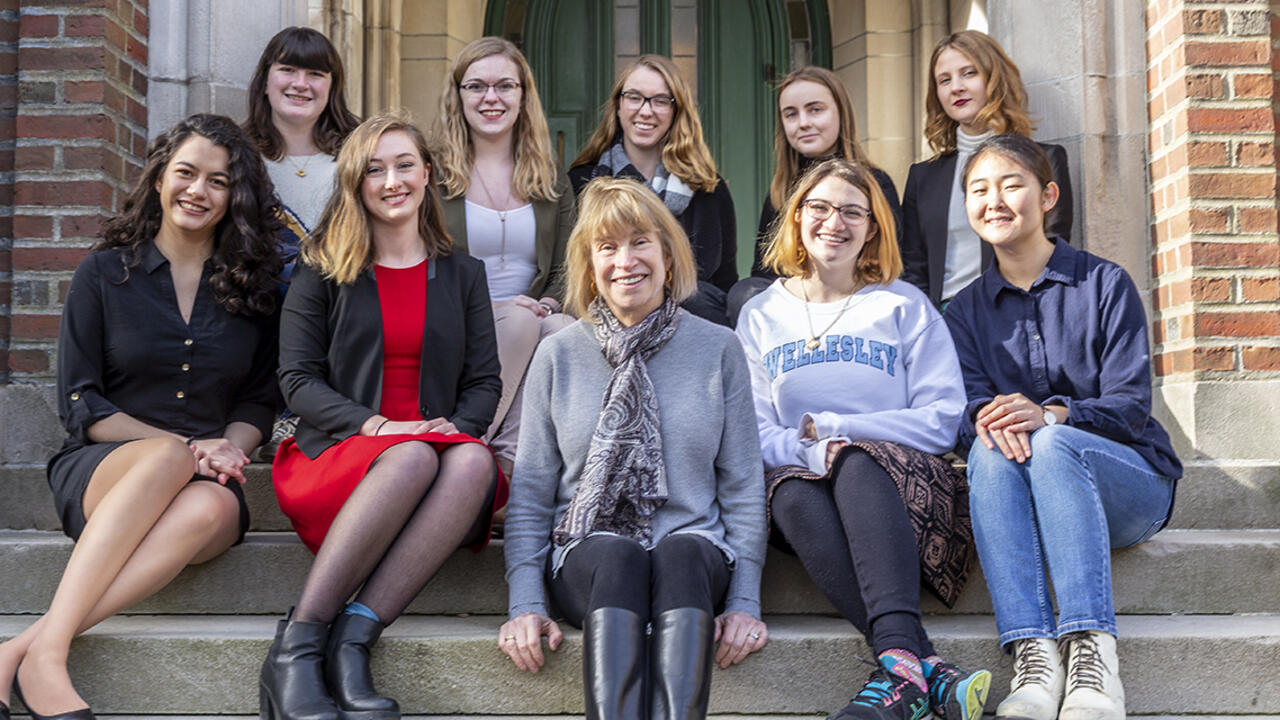 A group of nine students sit and their scholarship donor sit on steps