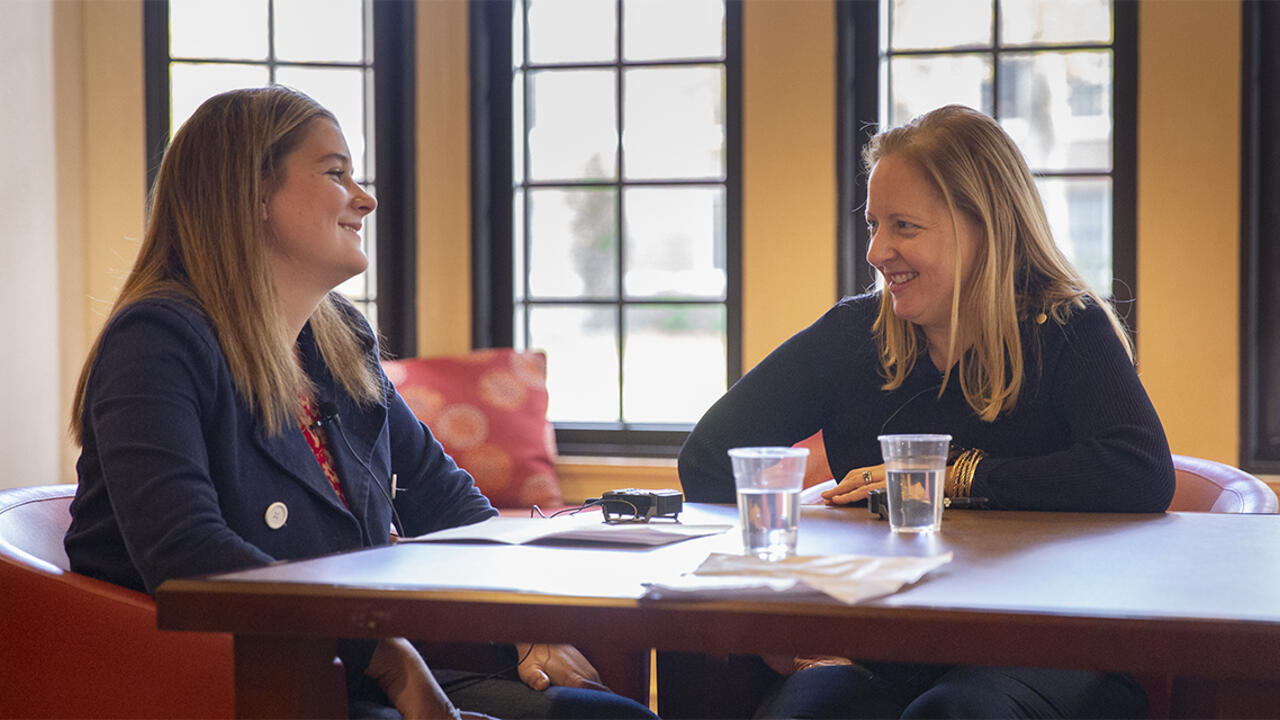 Two people sit together at a table and have a conversation.