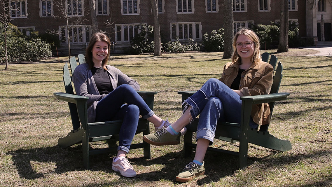 Two students sit in chairs in the academic quad.