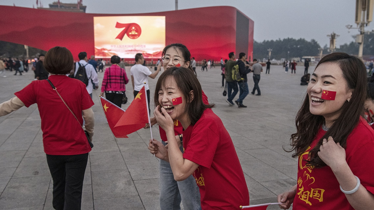 Chinese tourists wear 70th anniversary t-shirts as they stand near a large screen set up for the 70th National Day celebrations 