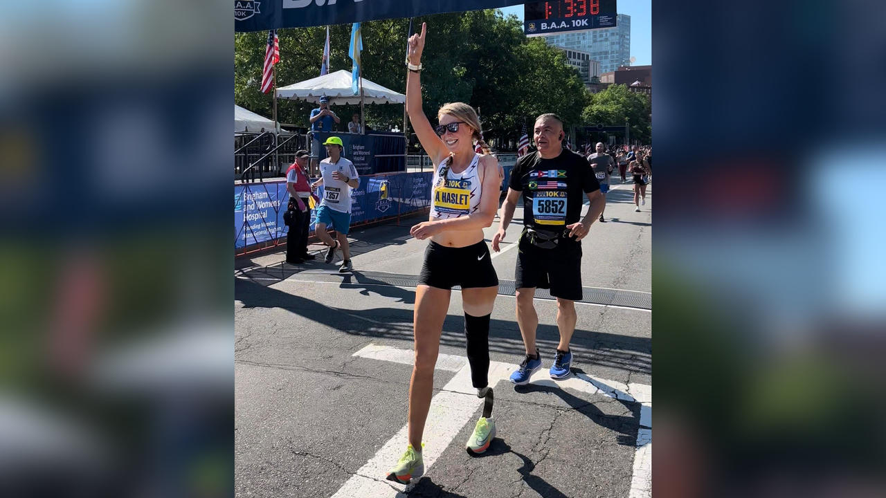 Adrianne Haslet crosses a finish line, holding up her right hand in exaltation.