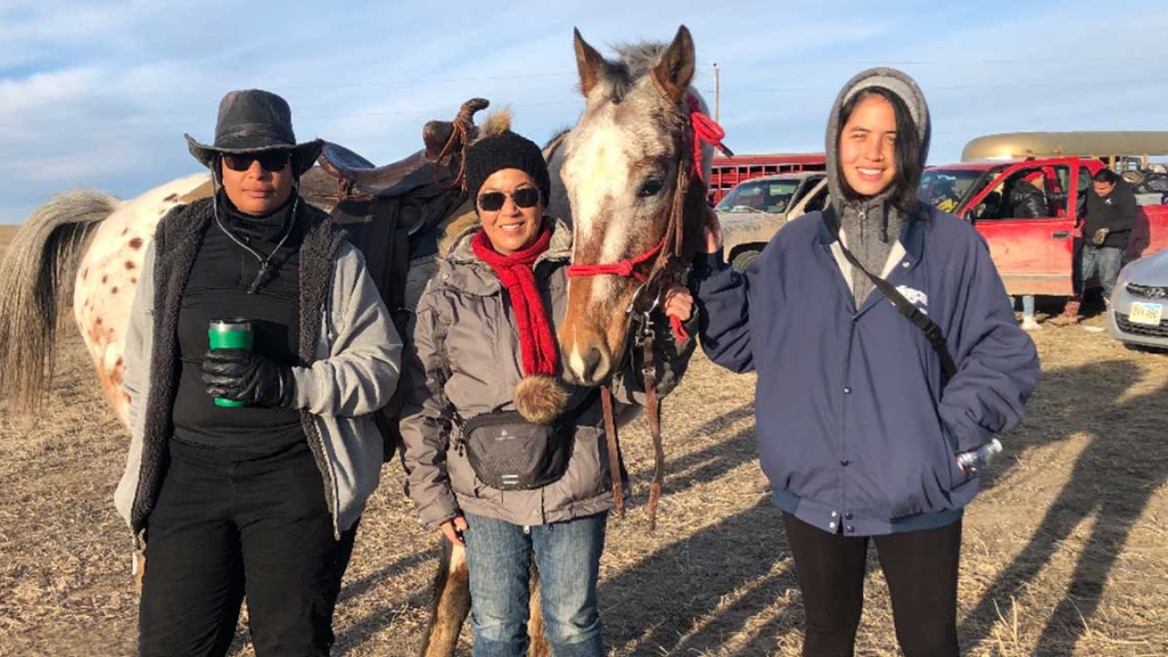 A professor and two alumnae stand with a horse