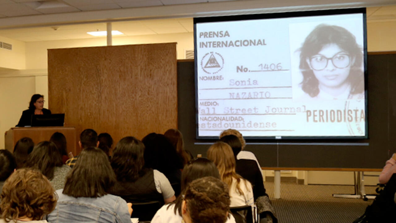 Sonia Nazario, a journalist, speaks to a room of students. On a projector there is an image of her press pass.