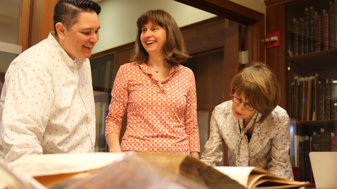 Three members of the archives and special collections staff look at a book.