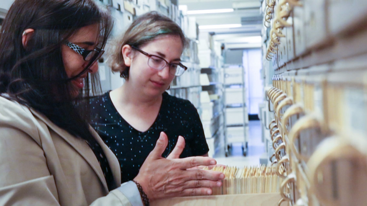 Two women look at a card catalogue in the archives. 
