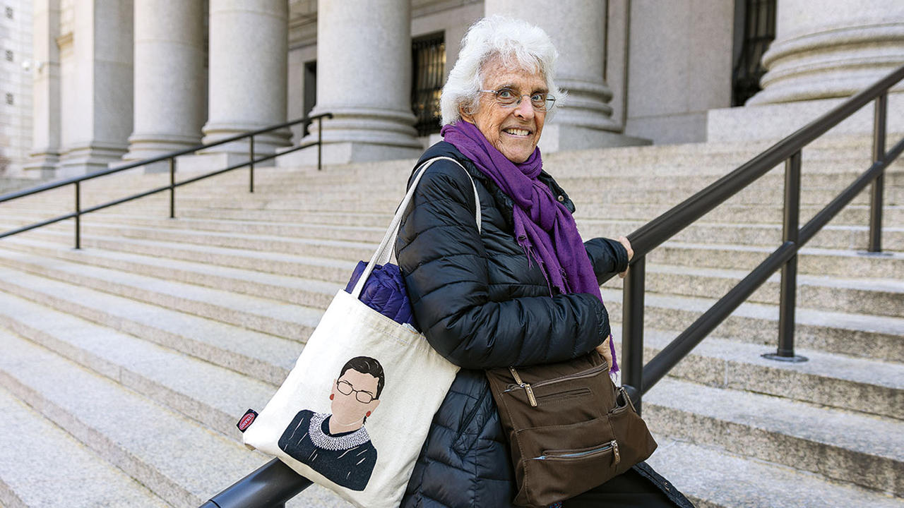 Nancy Stearns ’61 on the steps of the Thurgood Marshall U.S. Courthouse in New York City, holding a Ruth Bader Ginsburg tote bag