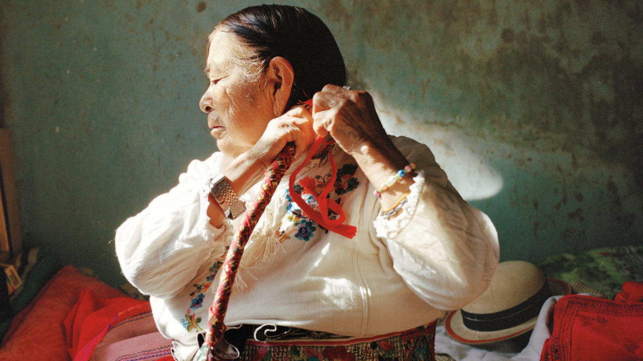 A photo of an older Hispanic woman braiding her long hair. 