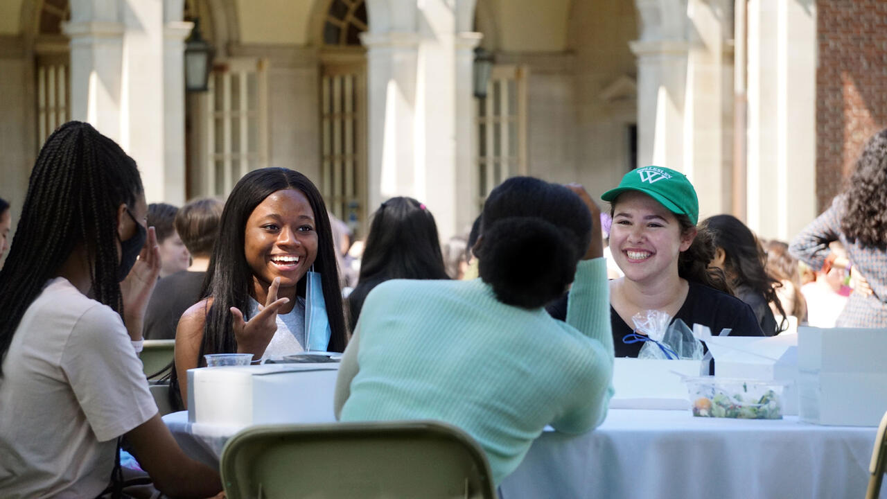 students smiling and eating together at an outdoor table