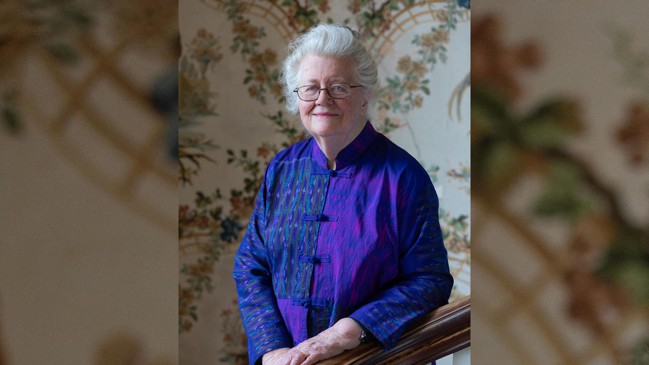 Peggy McIntosh on Cheever House’s grand staircase with original wallpaper and bannister dating from 1894.