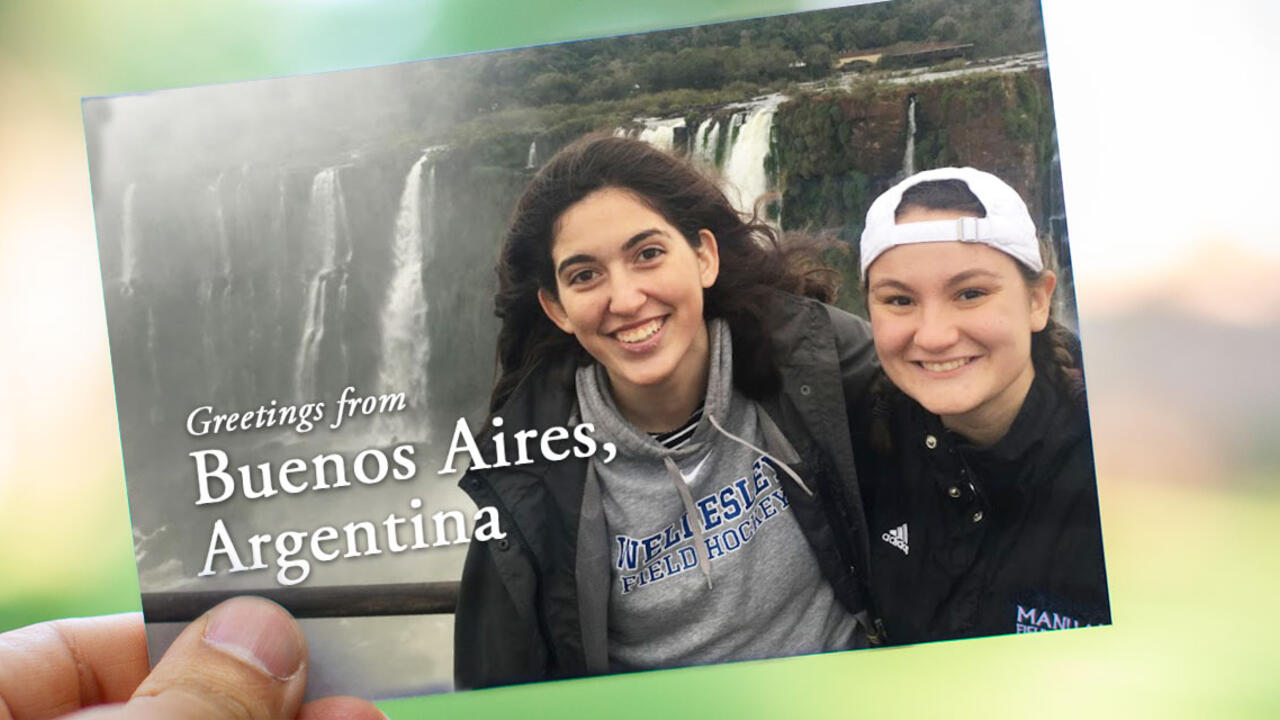 On a postcard, two students stand in front of a waterfall in Buenos Aires. It reads, "Greetings from Buenos Aires, Argentina!"