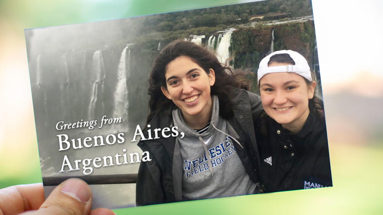 On a postcard, two students stand in front of a waterfall in Buenos Aires. It reads, "Greetings from Buenos Aires, Argentina!"