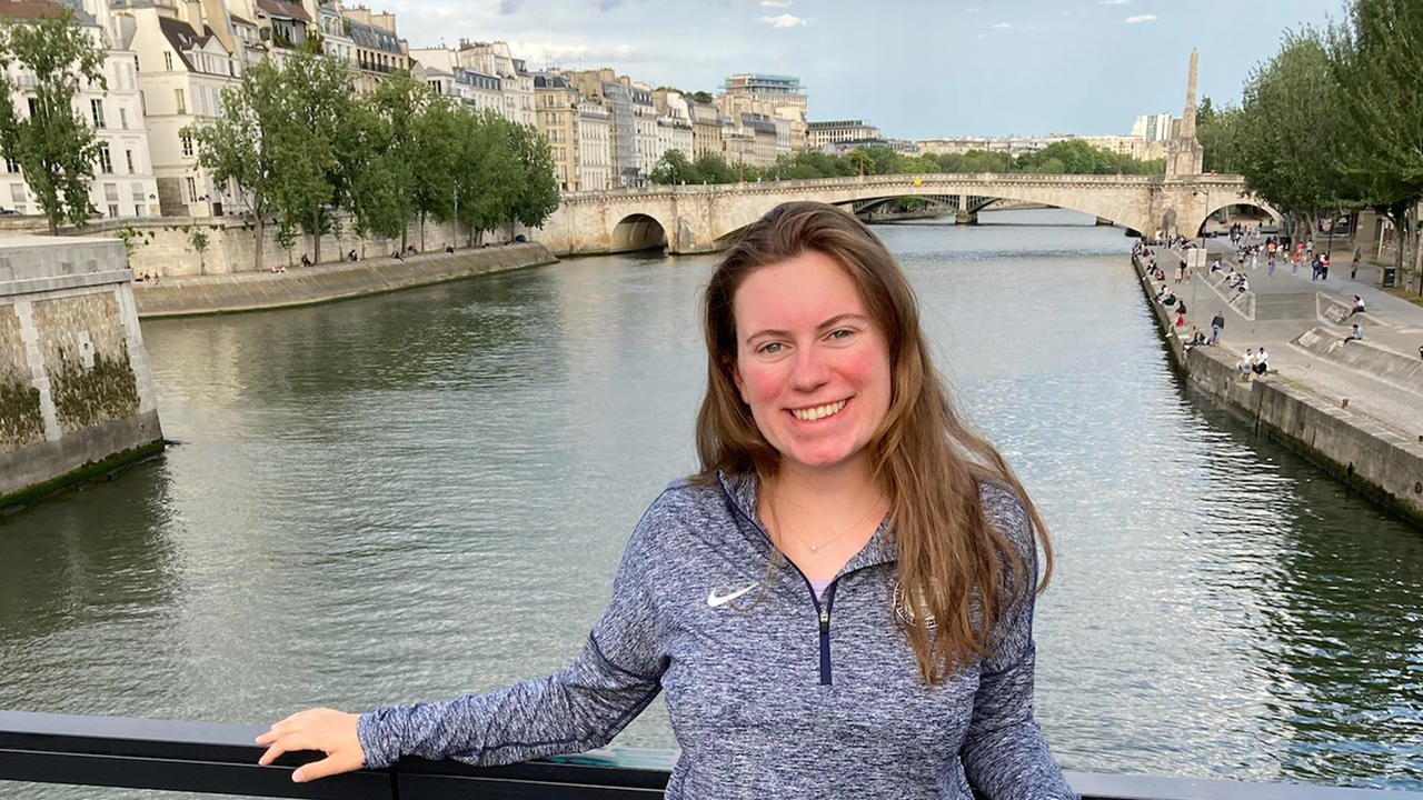 Rosalind Lucier ’22 stands in front of a channel of water with historic buildings behind her.