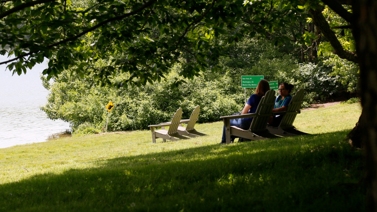Two people sit by lake waban near signs that read the names of cities around the world.