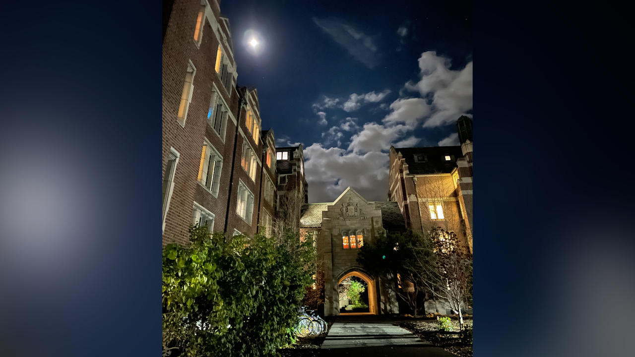 Campus building with a full moon lighting the sky and making night clouds visible.