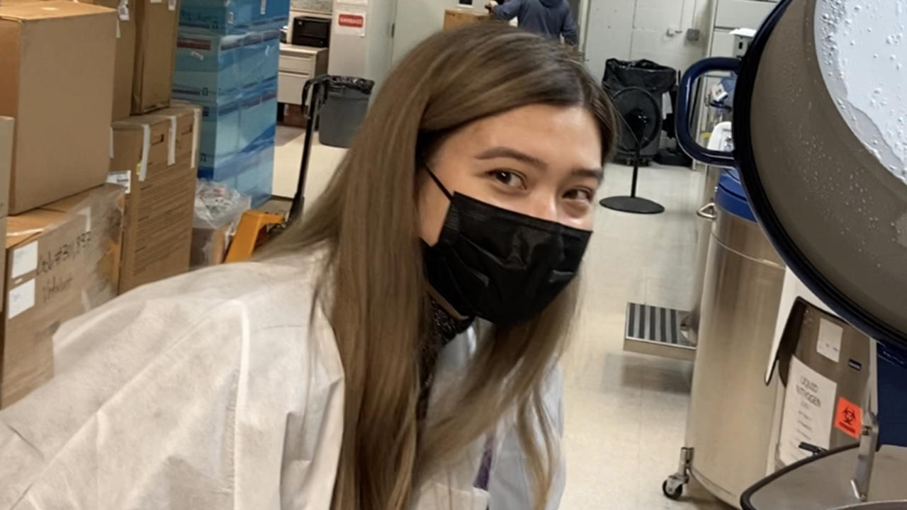 Kathryn Cross in a lab coat and black face mask looks at camera.