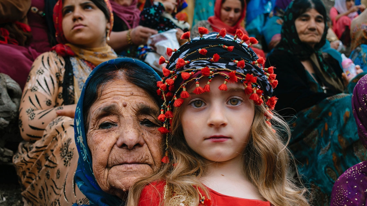 An older woman and young child look directly into the camera. They wear bright traditional kurdish clothing.