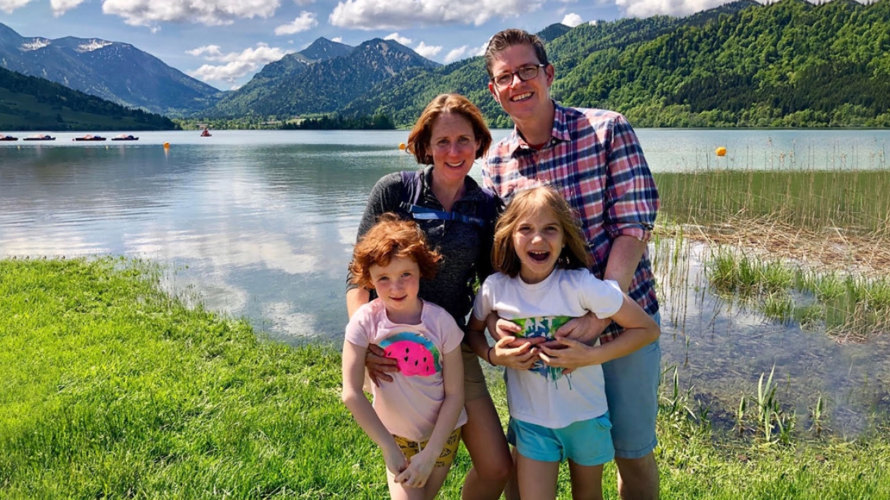 Two professors and their daughters stand in front of a lake.