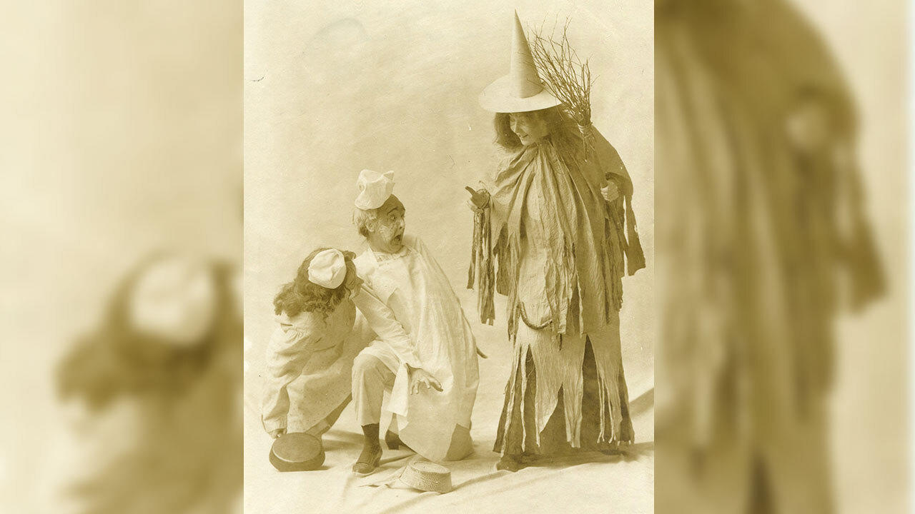 A theater photo from 1906 showing three students re-enacting a scene. The student at right is dressed as a witch.