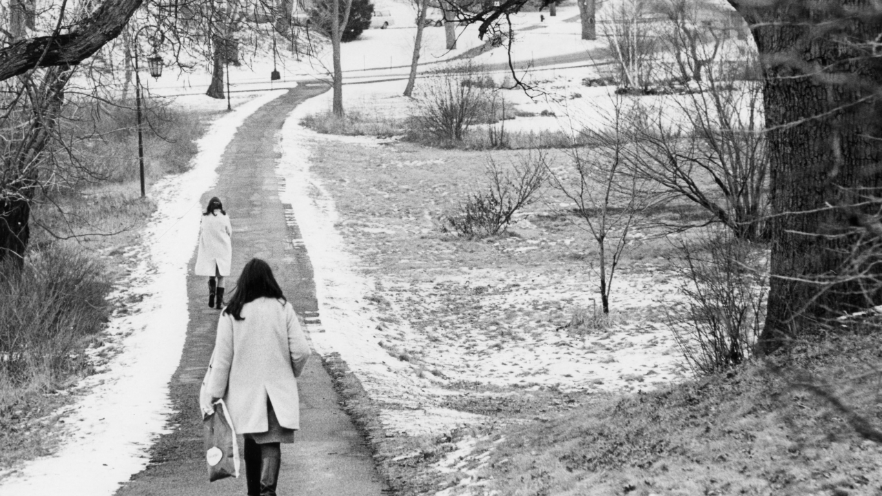 Two students walk a path at Wellesley College. There is a dusting of snow.