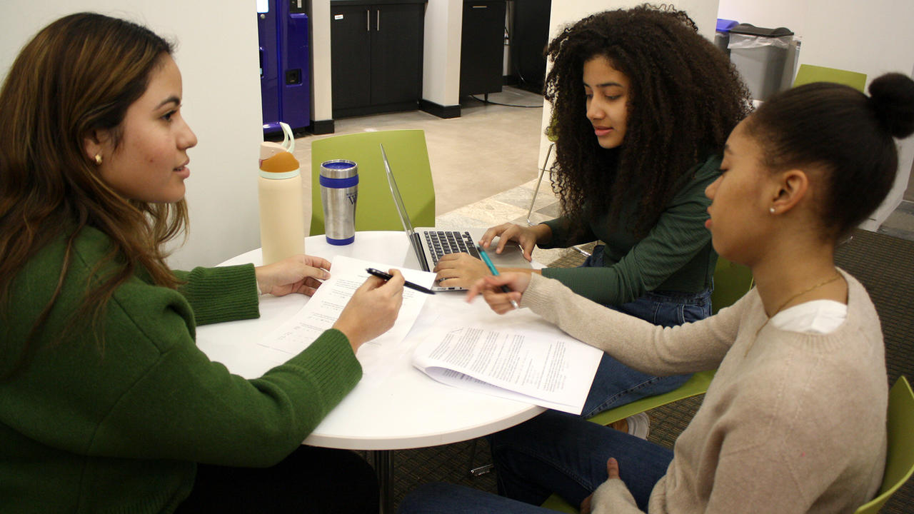 Three students sit at a table looking over papers.