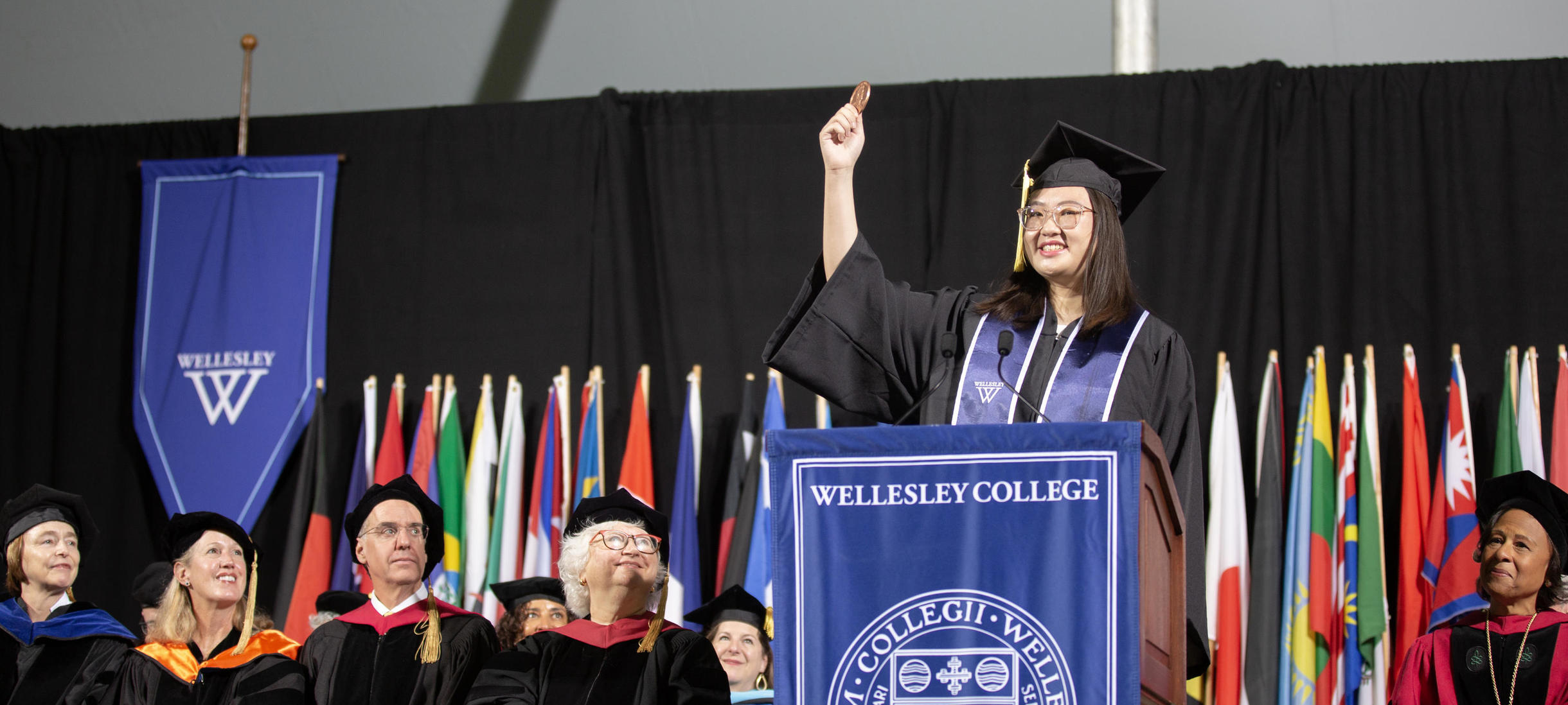 Student speaker Charlize Chen hold a giant penny aloft at the podium