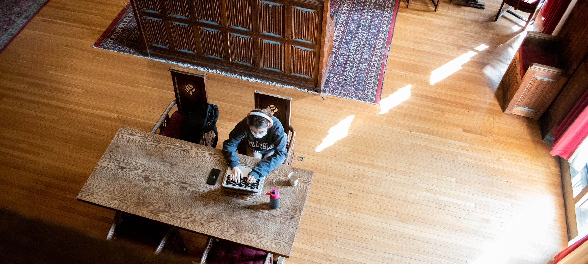 Picture of student, library, studying, oriental rugs, wood floors, sunlight.