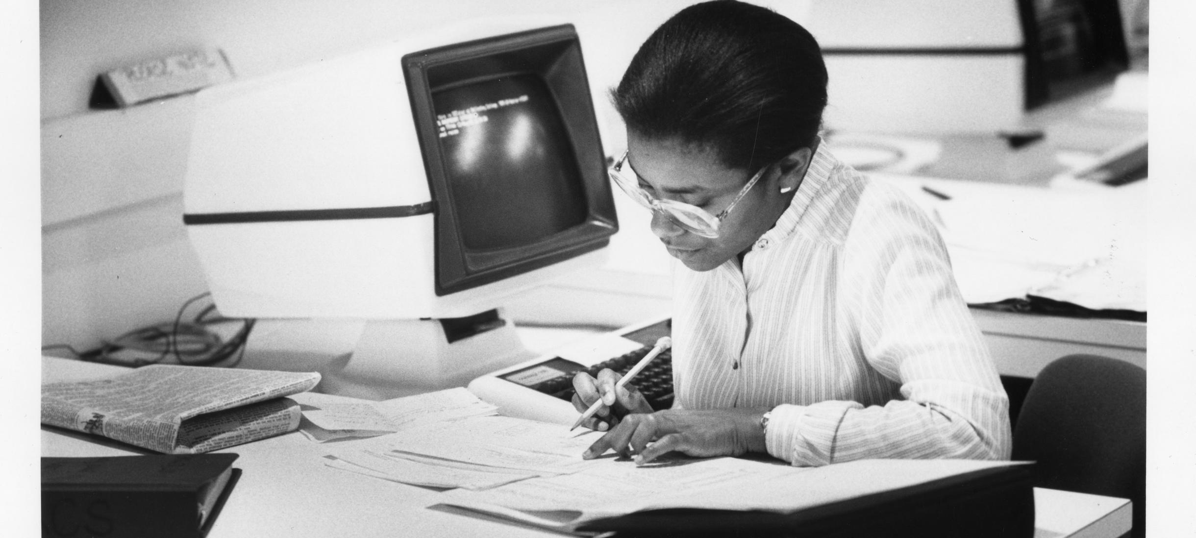 A black-and-white photograph of a Black Wellesley student working in the computer center in the library, taken circa 1975-85.