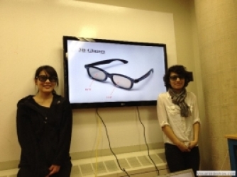 Tiffany Lin '12 and Irene Roman '13 stand in front of a screen with a photo of 3D glasses. 